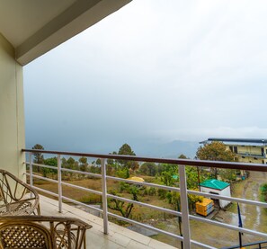 A balcony with wicker chairs, a view of a green landscape, and a building with a green roof.