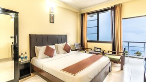 A hotel room with a large bed, a desk, a chair, a balcony with a view, and a ceiling fan. - Flutter Hotels & Resort (Lansdowne)