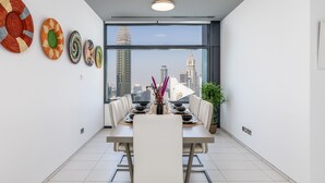 Un espace de restauration moderne offrant une vue panoramique sur la ville, une grande table à manger pouvant accueillir six personnes et des œuvres d’art décoratives murales.