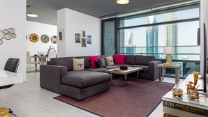 Un salon moderne avec un canapé d’angle gris, une table basse et une grande fenêtre donnant sur la ville.