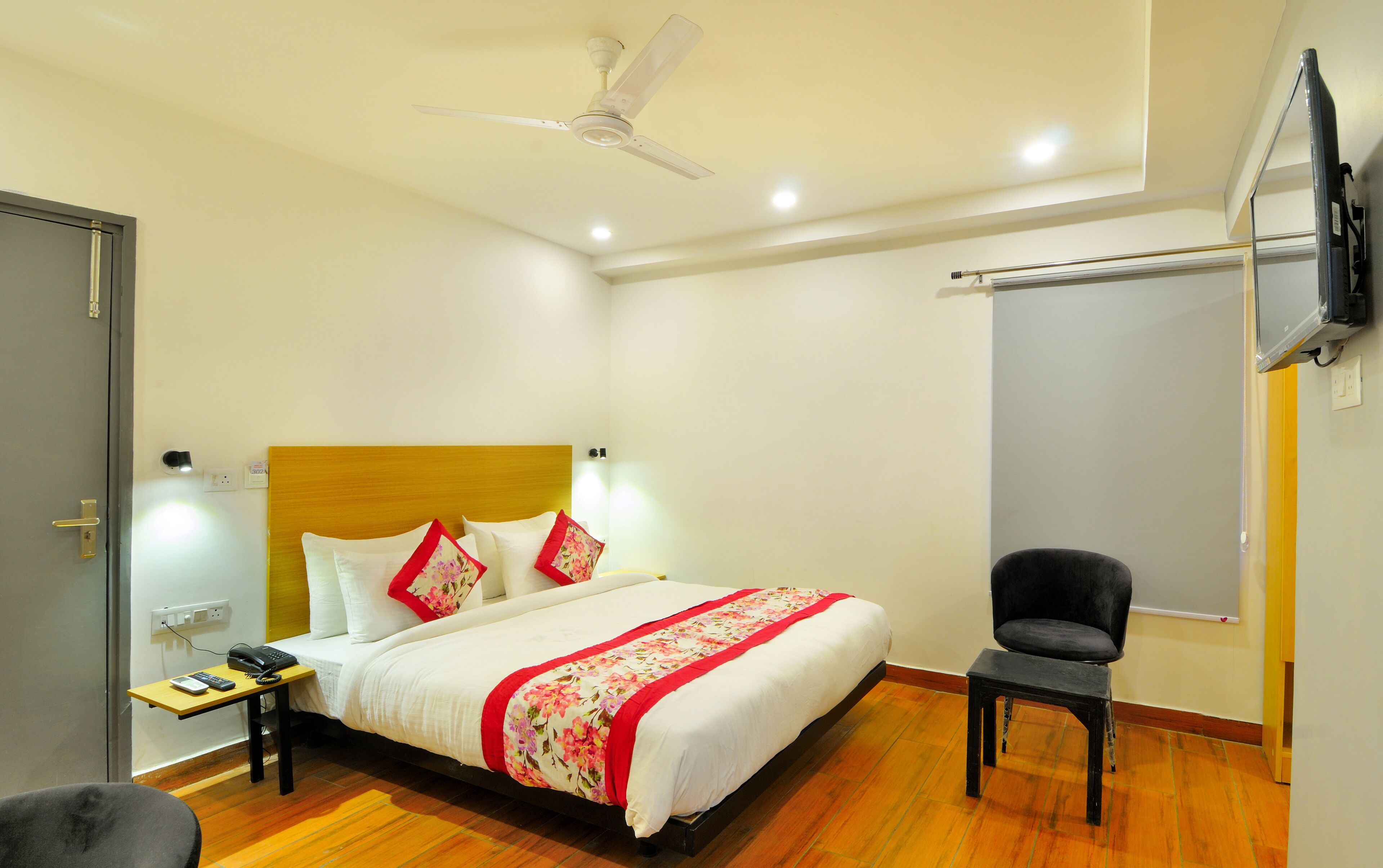 Quarto de hotel com cama, mesa de cabeceira, cadeira e ventilador de teto.
