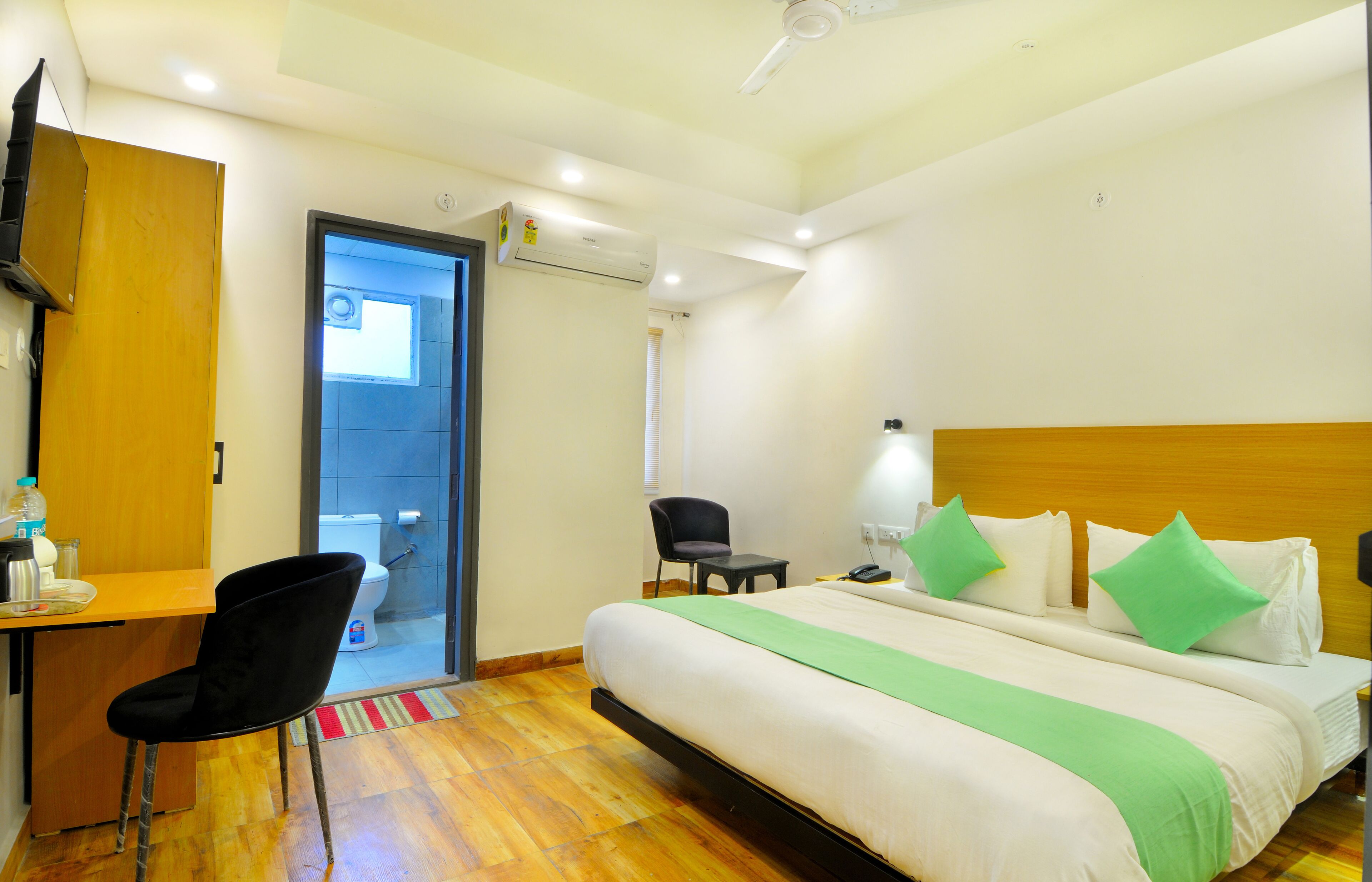 A hotel room with a bed, a desk, a chair, and a bathroom visible through an open door.
