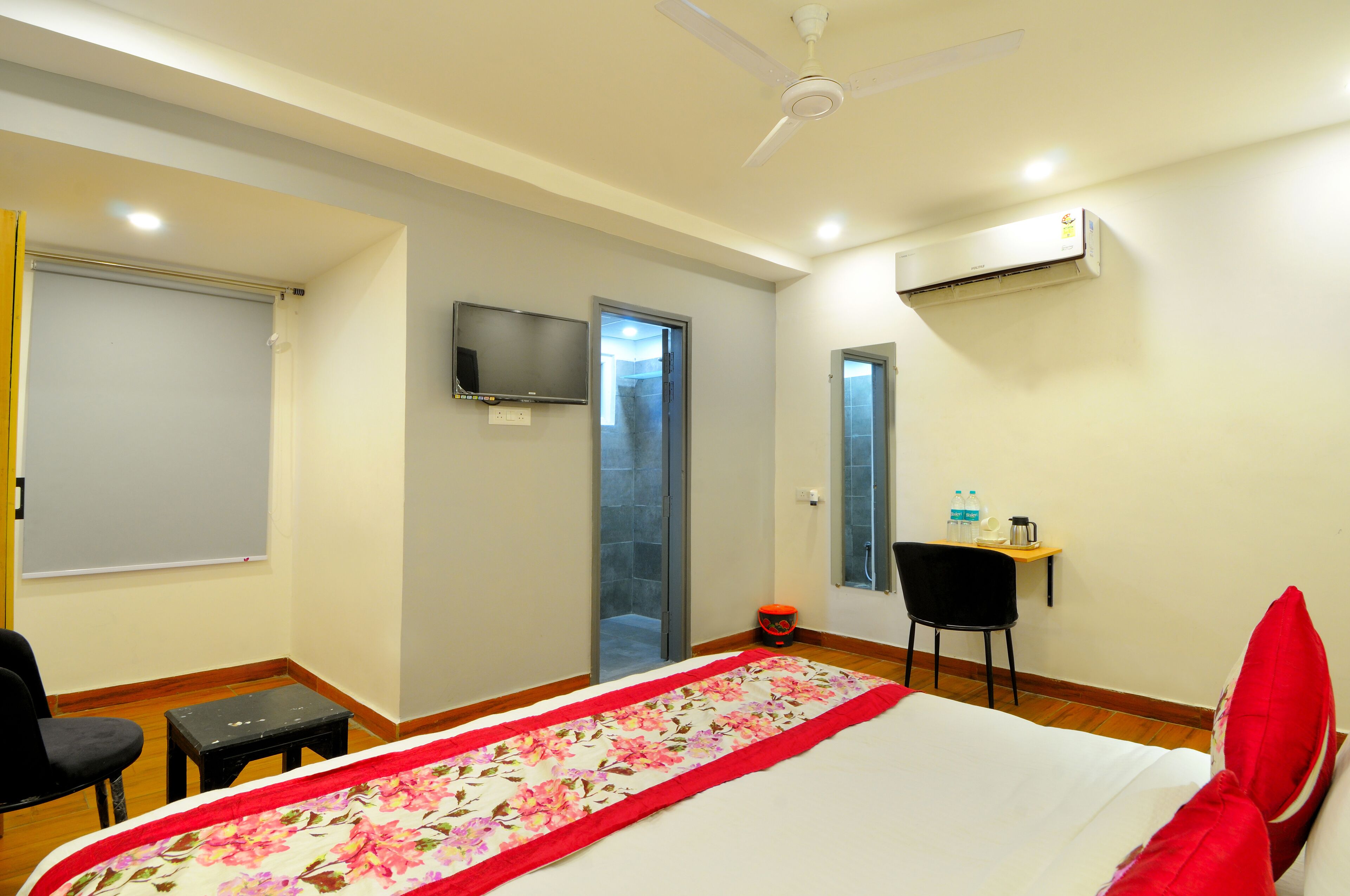 A hotel room with a bed, a desk, a chair, a TV, and a shower.