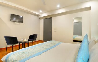 A hotel room with a bed, a TV mounted on the wall, two chairs, a small table, and a door.