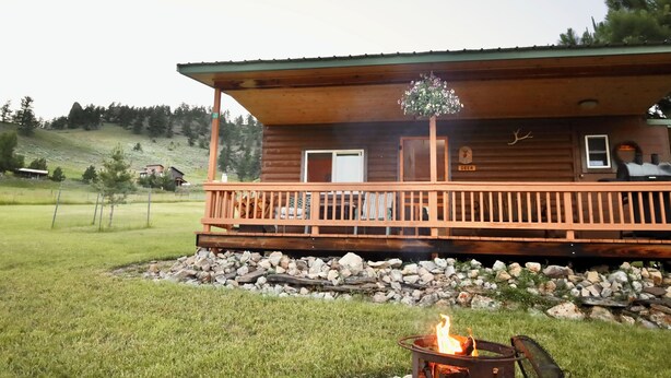 En træhytte med veranda, bålsted og et skilt der viser hjort.