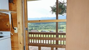 En trædør, der fører ud til en balkon med udsigt over et grønt landskab og bjerge.