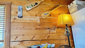Et interiør af en træhytte med trævæg, en træpagaj, en lampe, et bord med snacks og et vindue med persienner.