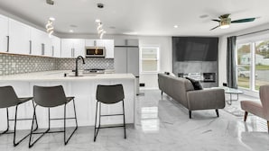 Een moderne keuken met een centraal eiland, barkrukken, een inbouwoven en een groot raam.