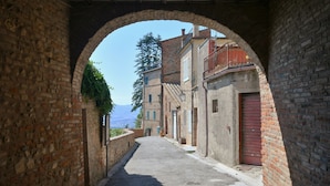 A narrow alleyway with brick buildings, a red door, and a clear sky. - Fontesecca (Citta della Pieve)