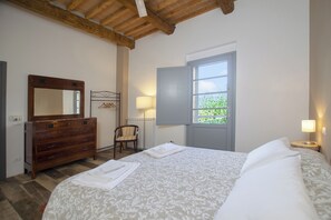 Un dormitorio con un aparador de madera, una cama con colcha estampada, un ventanal con vistas y una silla.