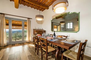 Un comedor con una mesa de madera dispuesta para cuatro personas, un espejo grande y vistas a través de puertas de cristal.