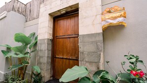 A wooden door with a metal latch, a small step leading up to it, and a wall-mounted shelf with decorative items. - Taman Bali Villa Dewi Sri (Legian)