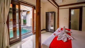 A hotel room with a bed, a sliding glass door to a pool, and a wardrobe. - Taman Bali Villa Dewi Sri (Legian)