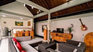 A spacious living area with a sofa, wicker furniture, a wooden cabinet, and a television. - Taman Bali Villa Dewi Sri (Legian)