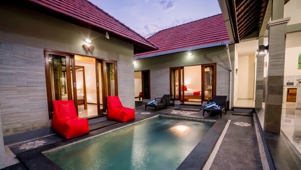 A modern pool area with red chairs, a lounge, and a bedroom with a red bed. - Taman Bali Villa Dewi Sri (Legian)