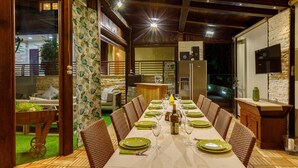 A dining area with a long table set for a meal, surrounded by wicker chairs.