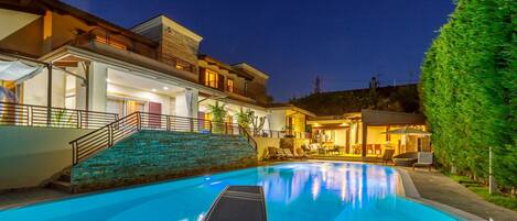 A modern poolside area with a stone staircase leading to a covered seating area.