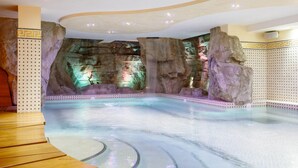 A spa area with a large indoor pool, rock formations, and a wooden bench.