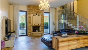 A spacious living room with a fireplace, a leather sofa, a wooden coffee table, and a staircase with a glass railing.