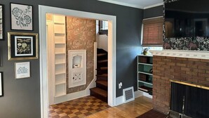 Un pasillo con piso a cuadros, una chimenea de ladrillo y una escalera que conduce a otra habitación.