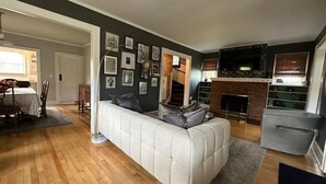 Una sala de estar con sofá, piso de madera, chimenea y comedor.