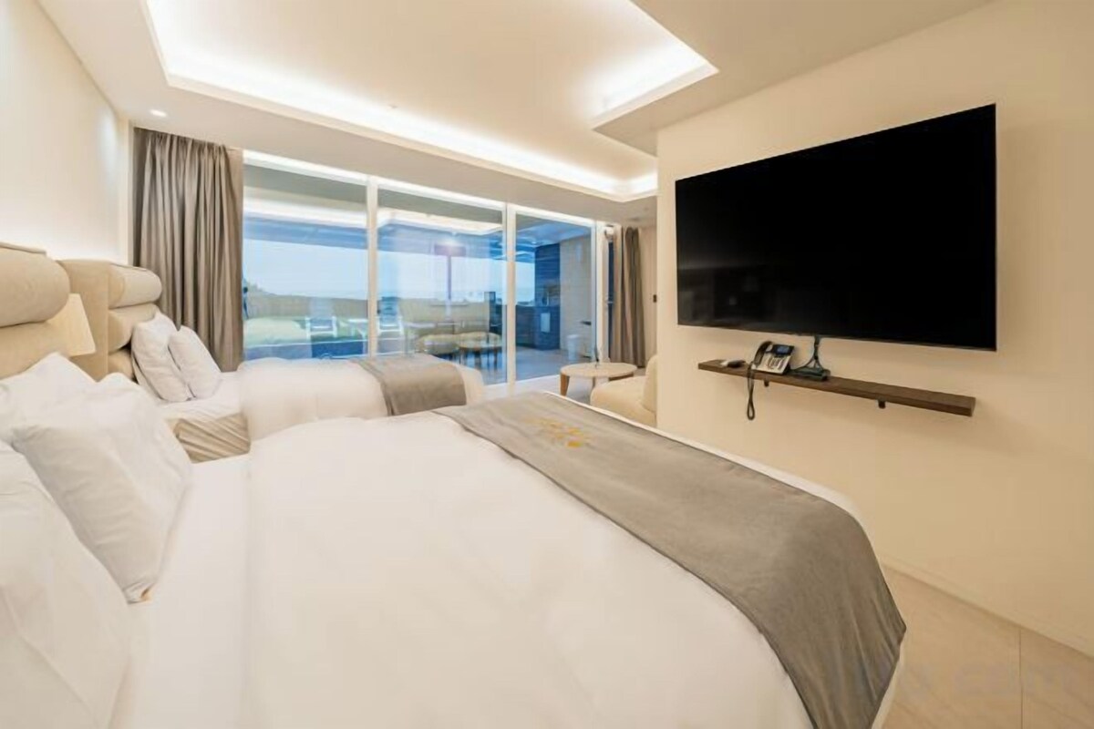 A hotel room with a large bed, a flat-screen TV mounted on the wall, and a balcony with a glass door.