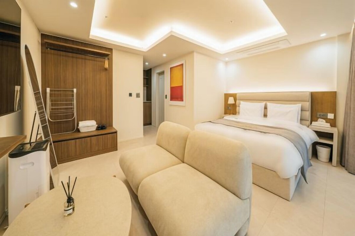 A modern hotel room with a bed, a sofa, a desk, and a shower area.