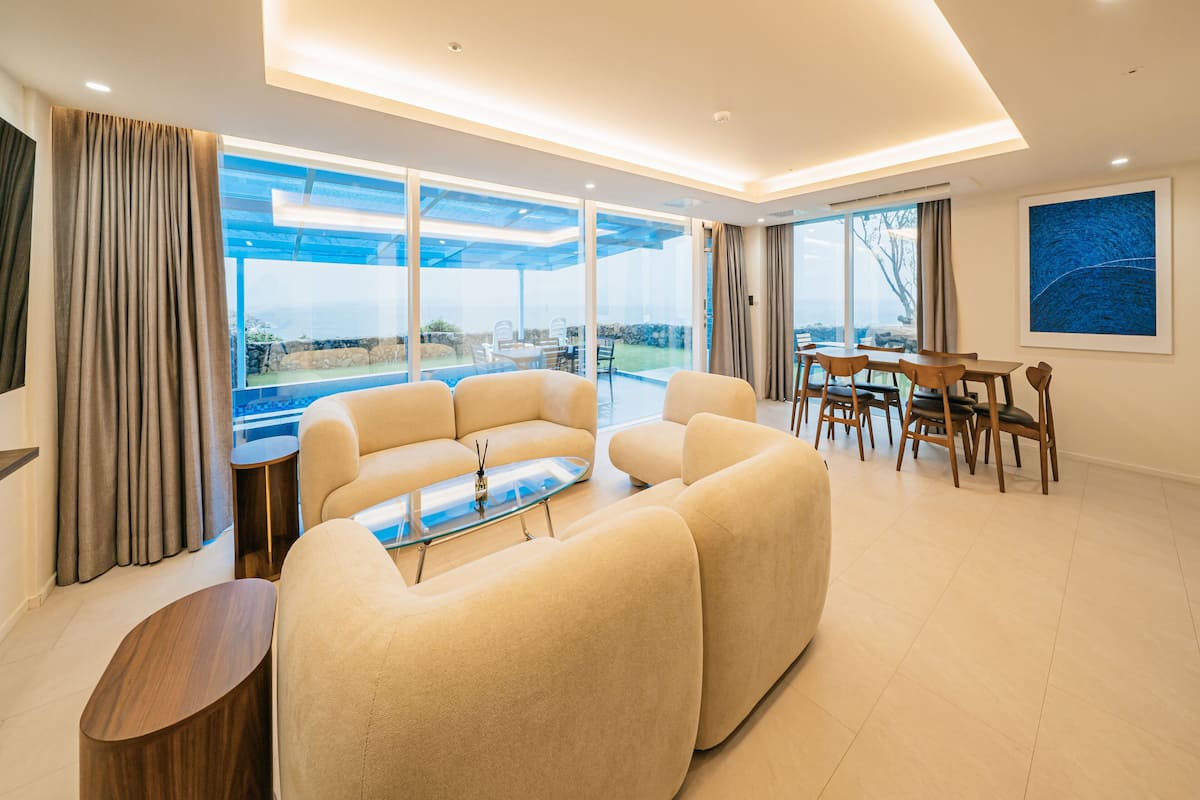 A modern living room with a sofa set, a glass coffee table, and a dining area with wooden chairs and a table.
