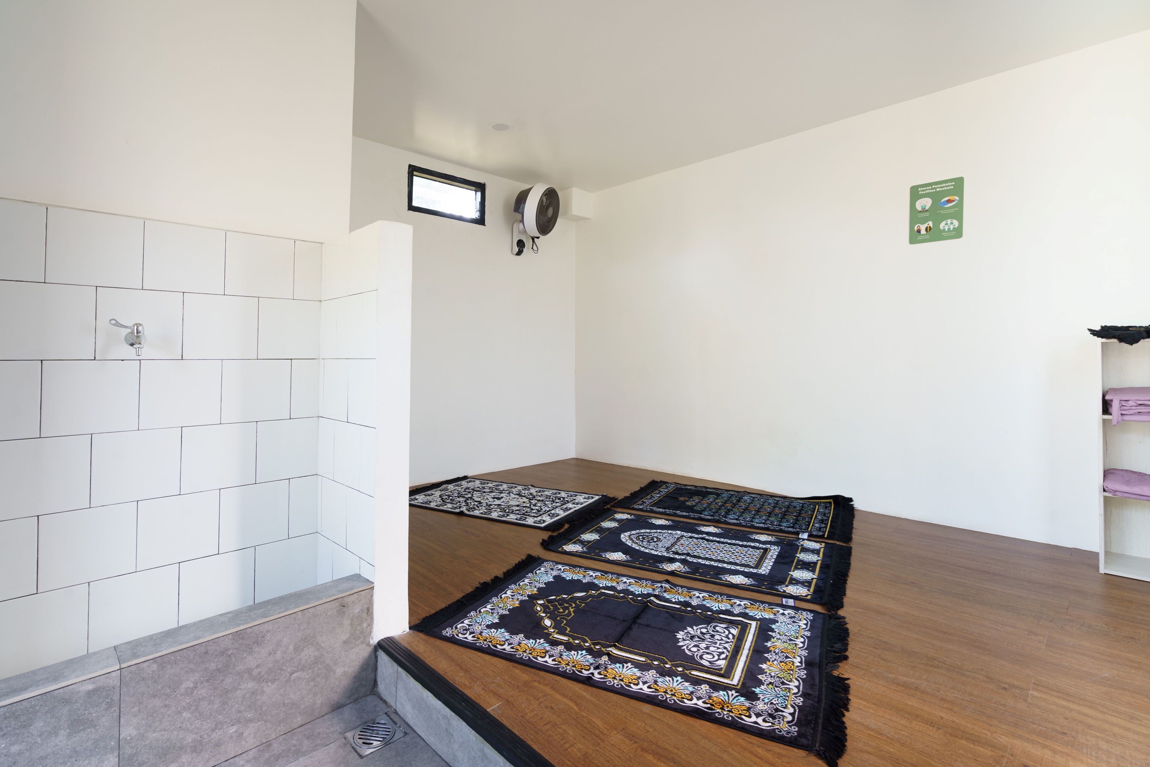 A room with a tiled wall, a wooden floor, and a prayer mat.