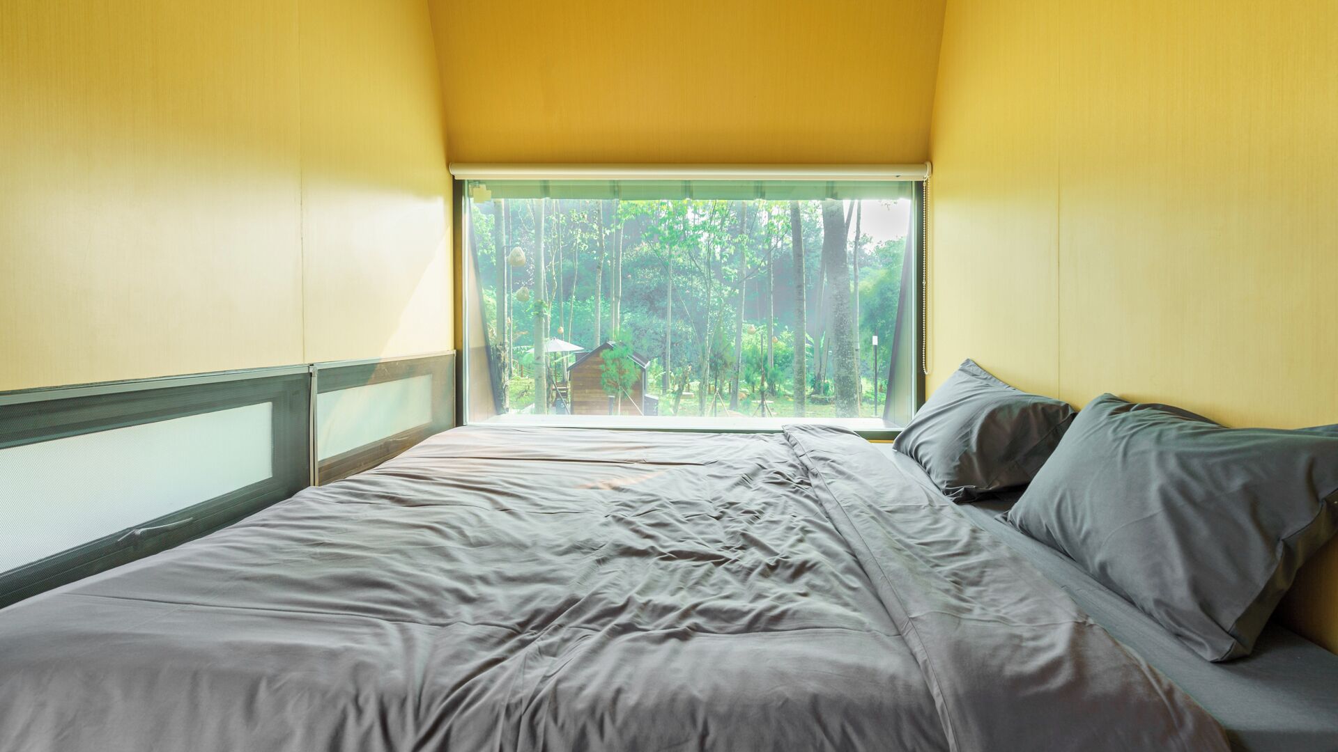 A bedroom with a bed, pillows, and a window with a view of trees.