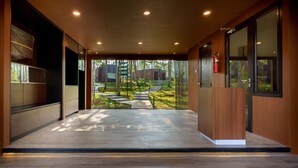 A modern hotel lobby with a wooden reception desk, a fire extinguisher, and a view of the outdoor garden area. - Bobocabin The Tavia Puncak (Megamendung)
