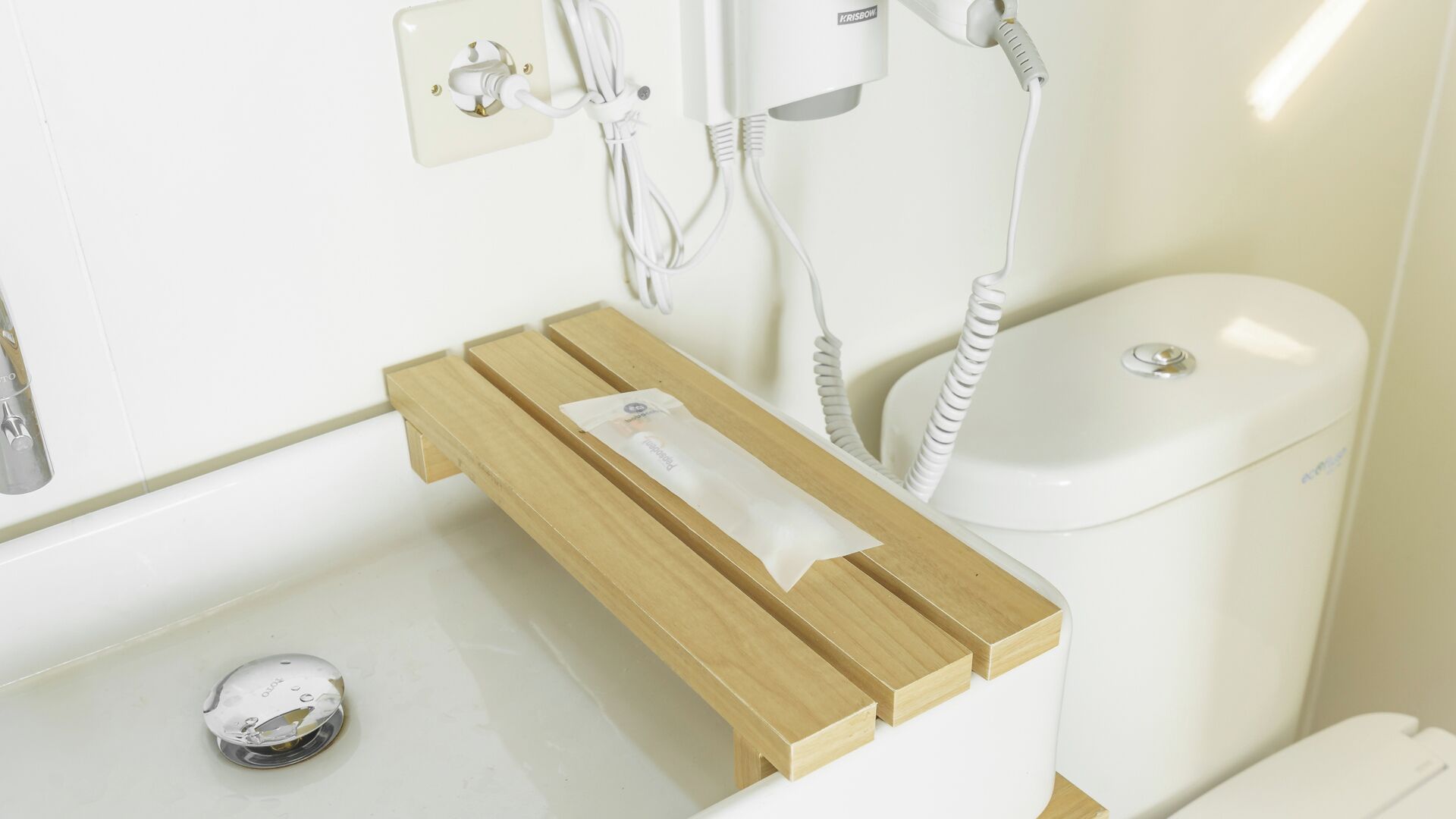 A bathroom with a wooden vanity, a toilet, and a hairdryer on a wall socket.