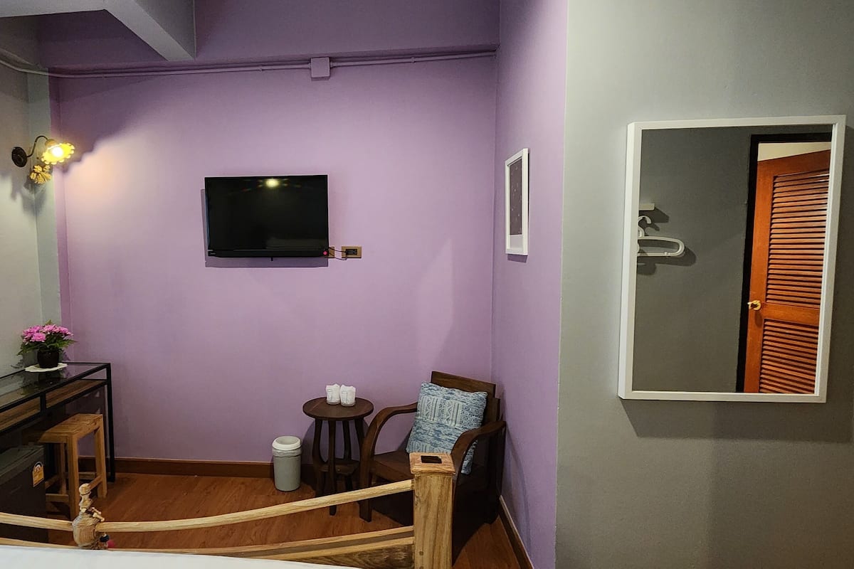 A bedroom with a bed, a TV mounted on the wall, a small table with a chair, and a mirror on the wall.