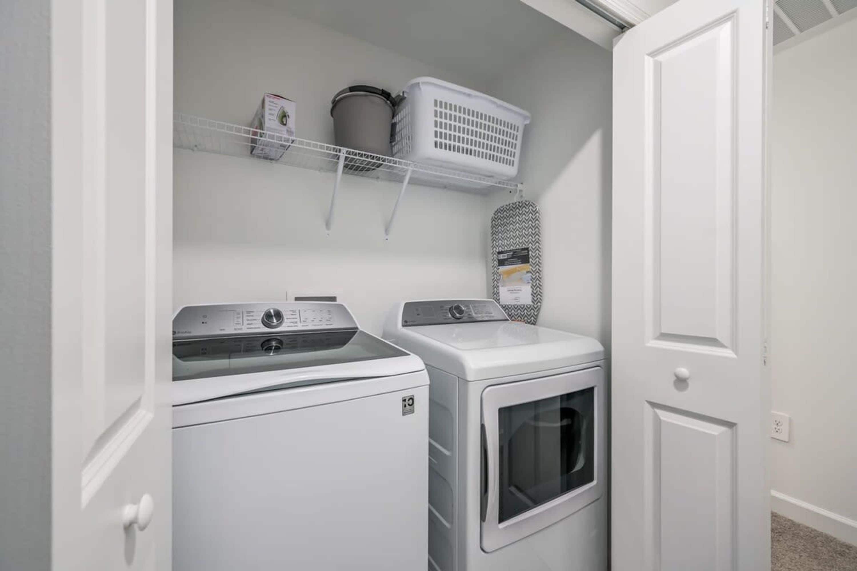 A laundry room with a front-loading washer and dryer, a shelf with laundry baskets, and a door.