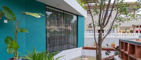 A modern building with a teal exterior, large windows, and a variety of potted plants.