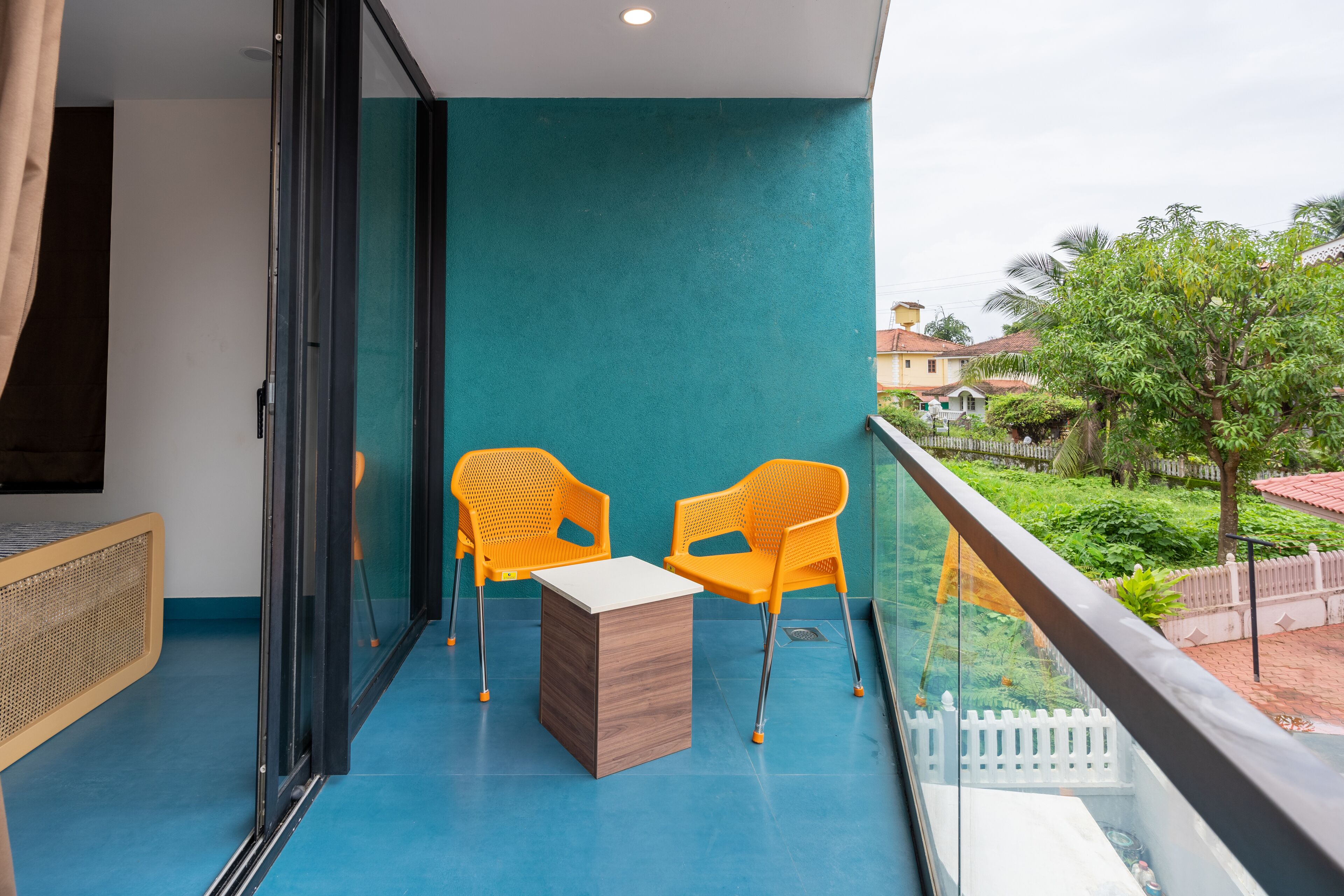 Un balcon avec un mur de couleur turquoise, deux chaises orange et une petite table en bois.