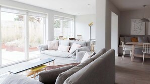 Una sala de estar moderna con un sofá, mesa de comedor y sillas. Hay un ventanal grande que proporciona luz natural y vistas al exterior.