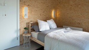 Un dormitorio con pared de madera, una cama con colcha blanca y una mesita de noche con una planta.