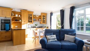 A cozy living room with a blue sofa, a kitchen with wooden cabinets, and a dining area.
