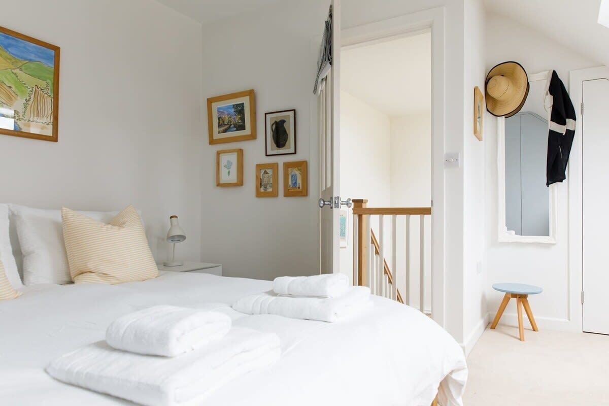 A neatly arranged bedroom with a bed, pillows, a bedside table, and a wall with framed pictures.