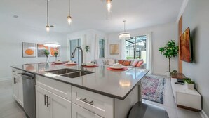 A modern kitchen with a central island, stainless steel appliances, pendant lighting, and a view to the outside.