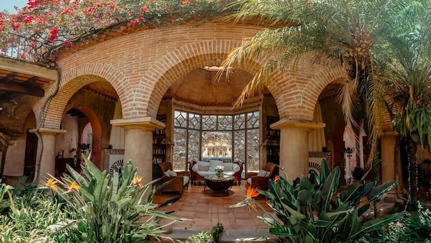 A courtyard with a central seating area, surrounded by brick arches and lush tropical plants.