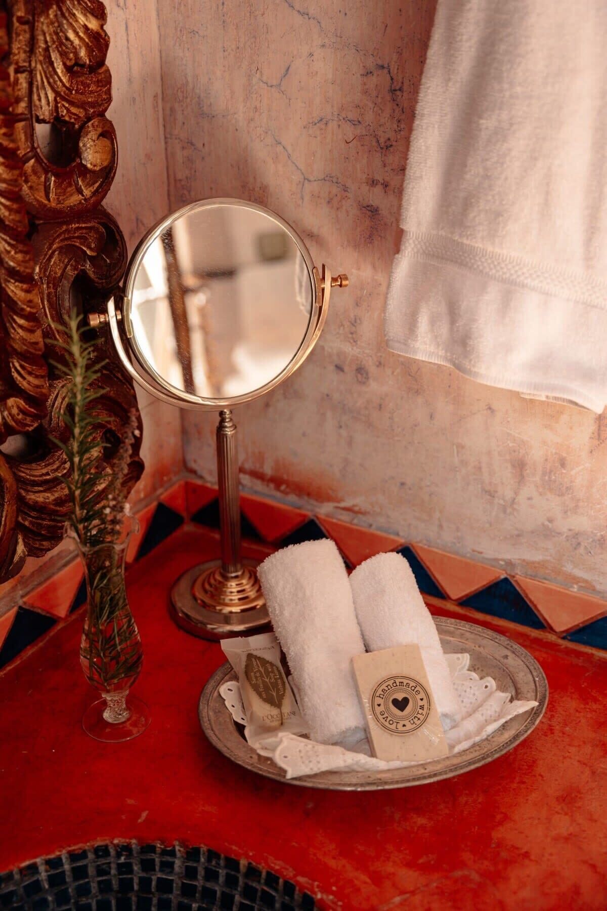 A bathroom vanity with a round mirror, a decorative vase, and a tray with towels and a soap bar.