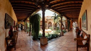 A covered outdoor area with tiled flooring, wooden benches, and potted plants.