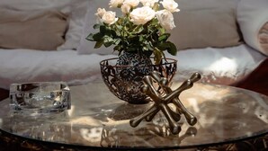 A room with a stone wall, a sofa, a vase with white flowers, and a decorative metal piece on a glass table.
