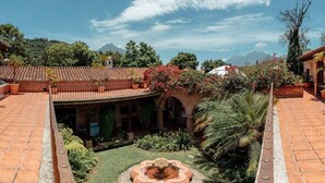 Un patio con una fuente, edificios con techo de tejas de arcilla y abundante vegetación.