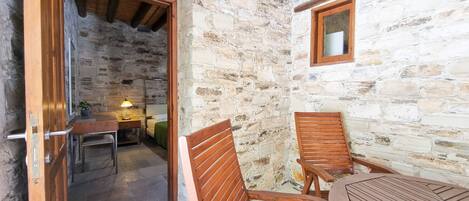 A rustic stone-walled room with wooden furniture, including a table and chairs, and a wooden door leading to another room.
