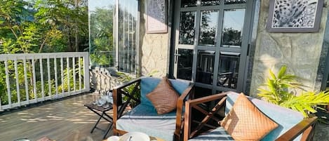 A covered outdoor seating area with a stone wall, wooden furniture, and a view of the outdoors.
