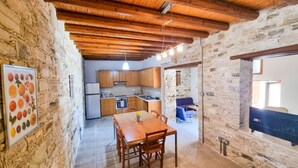 Une cuisine rustique avec des poutres en bois, des murs en pierre et un coin repas comprenant une table et des chaises.