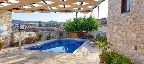 A stone pool with a pergola overhead, surrounded by potted plants and a stone wall. - Traditional Village Pool Apartment (Skarinou)